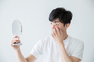 目やにが止まらない原因を特定し、結膜炎との見分け方や正しい対処法を決定するために、医師による診察や鏡を用いた症状の確認・指導を受けている男性の様子の写真